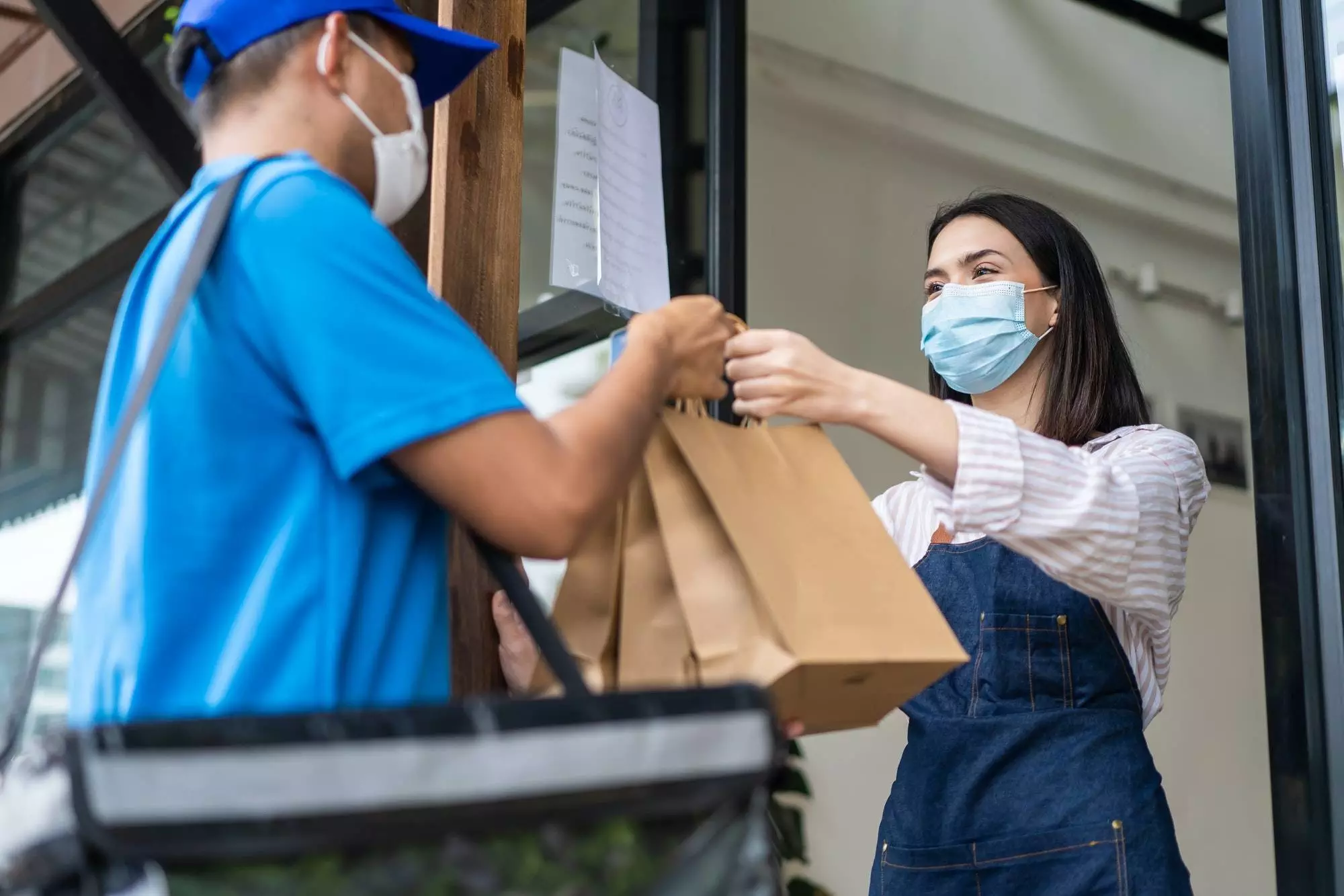 Asian waitress give takeaway foods bag to postman delivery for new normal lifestyles in restaurant