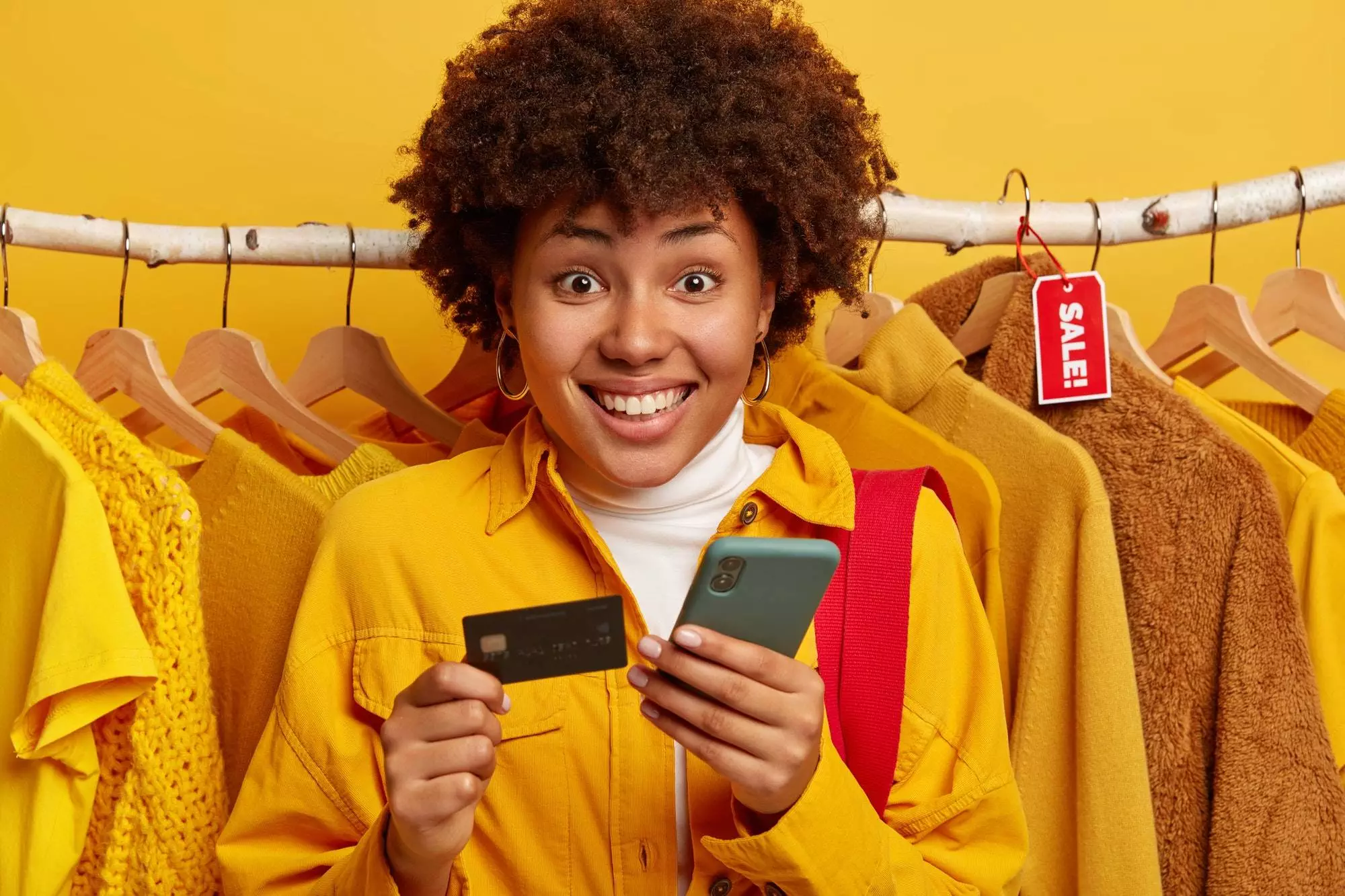 Pleasant looking Afro woman verifies bank account, pays online via smartphone, holds credit card, re