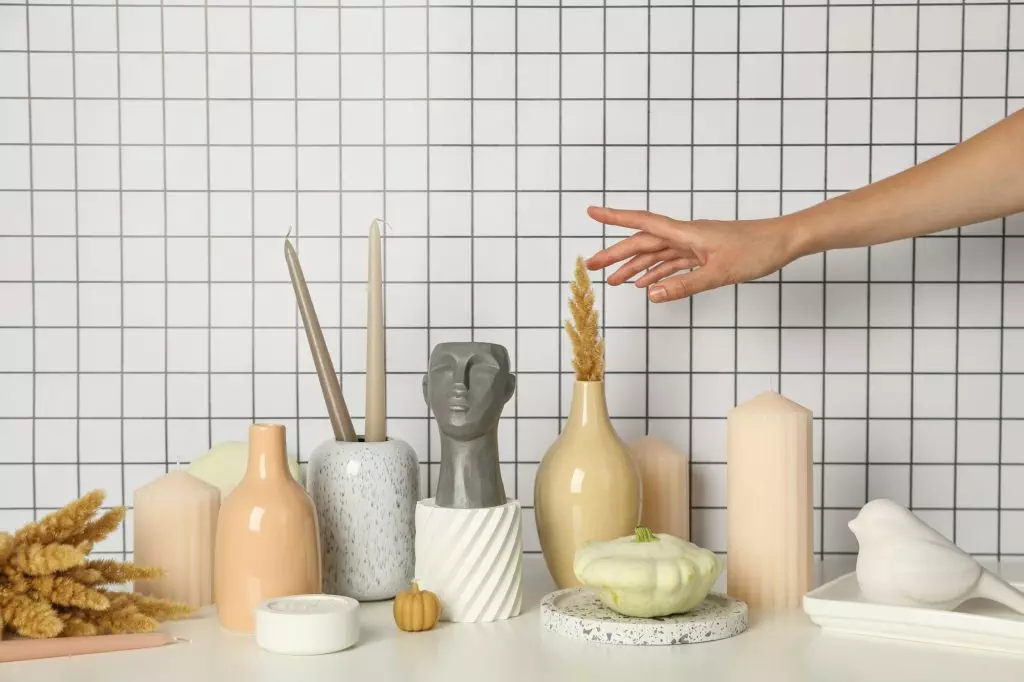 Candles, vases, figurines and female hand on light background